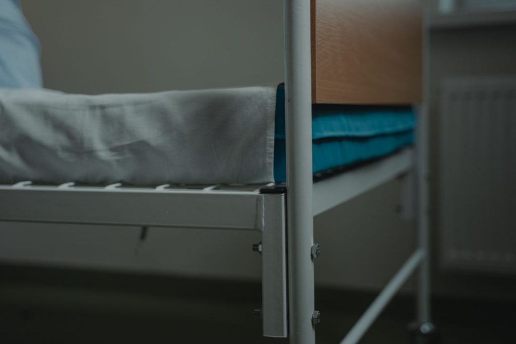 pexels-photo-6010874 Close-up view of a hospital bed with white linens and metal frame, indoors.